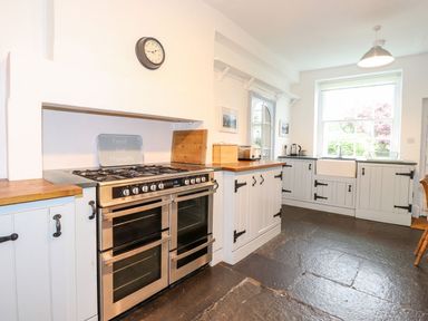 A kitchen with a stove oven, wooden countertops, cabinets, a clock on the wall, and a large window at Middletown in Keswick