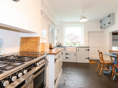 A kitchen with a gas stove wooden countertop white cabinets a window wooden chairs and a round table at Middletown in Keswick