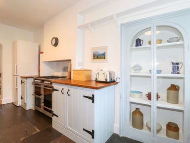 A kitchen with a stove, refrigerator, toaster, wooden countertop, and a glass-front cabinet with pottery at Middletown in Keswick
