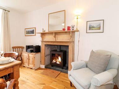 A living room with a wooden fireplace and fire stove a light blue armchair and wooden furniture at Middletown in Keswick