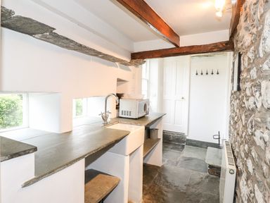 A narrow kitchen with stone countertop white sink microwave stone floor and exposed wooden beam at Middletown in Keswick