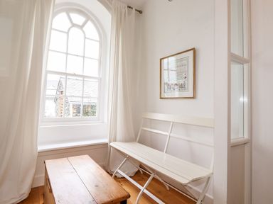 A room with a wooden chest as a table a white bench an arched window with white curtains and a framed picture on the wall at Middletown in Keswick