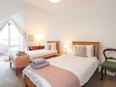 A bedroom with two single beds with pink throws and folded towels a wooden chest and a window with floral curtains at Middletown in Keswick