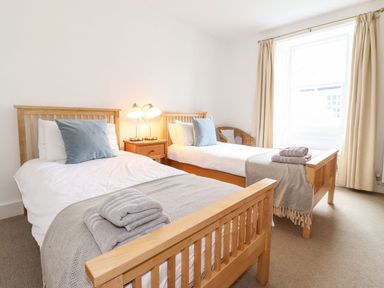 A bedroom with two wooden single beds with pillows and folded towels next to a window with curtains at Middletown in Keswick