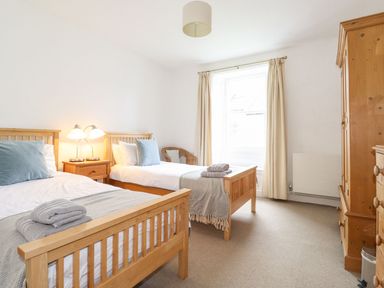 A bedroom with two single beds with wooden frames bedside table lamps a wicker chair a wooden wardrobe and a window with curtains at Middletown in Keswick