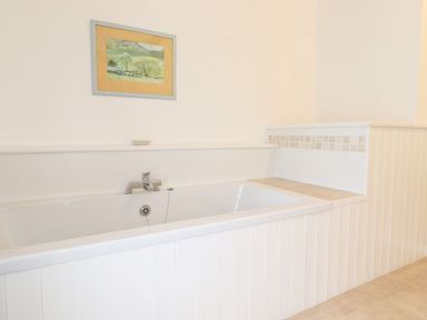 A white bathtub with a faucet and tiles on the side wall and a framed picture above at Middletown in Keswick