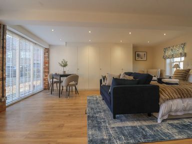 A room with a bed covered in blankets a dark sofa a dining table with chairs and large windows with blinds at Providence Court Near Easingwold