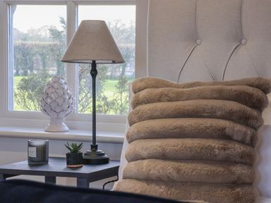 A bedside table with a lamp small plant and candle beside a bed with a furry pillow at Providence Court Near Easingwold