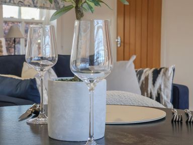 A dining table with two wine glasses a white plant pot and cutlery with a sofa and cushions in the background at Providence Court Near Easingwold