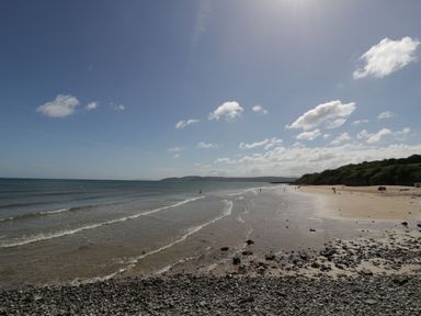 A beach with sand and pebbles along the shore with the sea and a partly cloudy sky near Ynys Uchaf Near Benllech