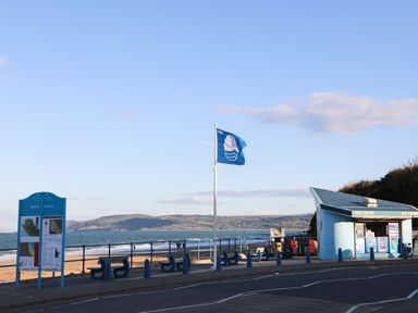 A beachside area with benches a blue flag an ice cream kiosk and a signboard near the sea at Ynys Uchaf Near Benllech