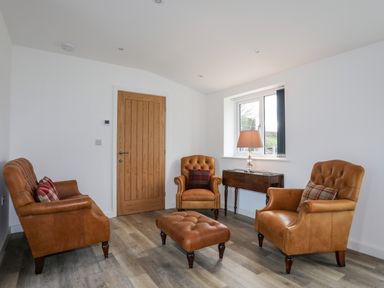 A sitting room with three leather armchairs a matching ottoman wooden side table and a lamp near a window at Ynys Uchaf Near Benllech