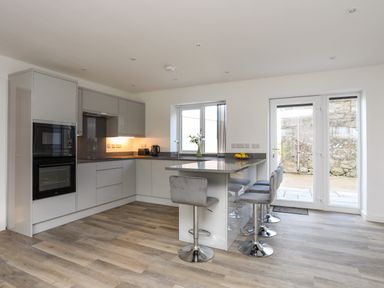 A modern kitchen with a breakfast bar and four stools near glass doors and a window at Ynys Uchaf Near Benllech