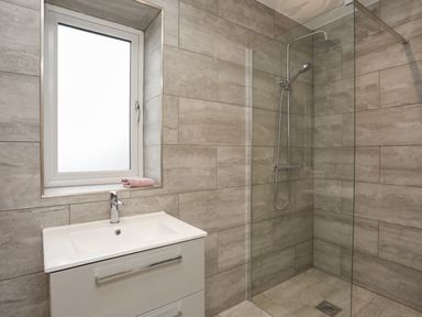 A bathroom with a sink under a window and a walk in shower with glass partition at Ynys Uchaf Near Benllech
