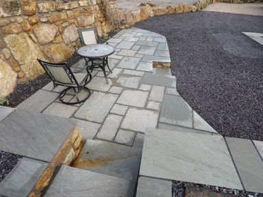 An outdoor stone patio with two metal chairs and a round table beside a stone wall at Ynys Uchaf Near Benllech