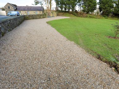 A gravel driveway next to a grass area with a stone building and a blue van in the background at Ynys Uchaf Near Benllech