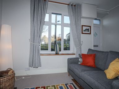A living room with a grey sofa with colorful cushions by a window with grey curtains and a floor lamp at Gwelfor in Harlech