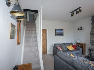 A living room with a staircase carpeted in grey two grey sofas with multicolored cushions and a stone fireplace at Gwelfor in Harlech