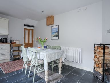 A dining area with a table and four chairs a vase with flowers and stacked firewood at Gwelfor in Harlech