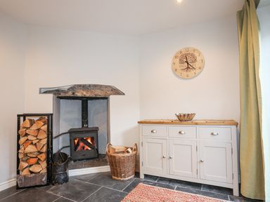 A room with a wood burning stove firewood basket wood storage cabinet and wall clock at Gwelfor in Harlech