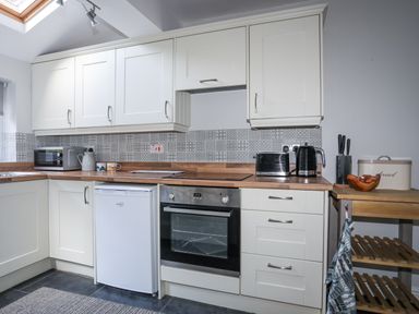 A kitchen with white cabinets black appliances a wooden countertop and a small wooden shelf at Gwelfor in Harlech