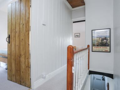 A hallway with a wooden door leading to a bedroom and stairs going down at Gwelfor in Harlech