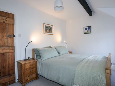 A bedroom with a wooden bed and side tables with lamps and paintings on the wall at Gwelfor in Harlech