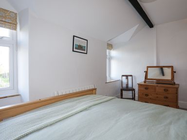 A bedroom with a wooden bed a chair a wooden dresser with mirror and two windows at Gwelfor in Harlech