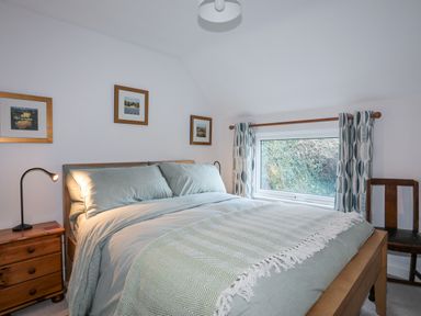 A bedroom with a bed next to a window a bedside table with a lamp and framed pictures on the wall at Gwelfor in Harlech
