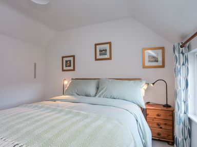 A bedroom with a bed, bedside table, lamp, three framed pictures on the wall, and curtains at Gwelfor in Harlech