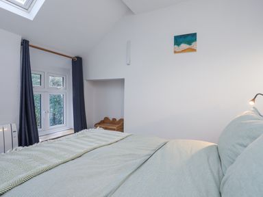 A bedroom with a bed covered in light green bedding a window with dark curtains and a small wooden desk in an alcove at Gwelfor in Harlech