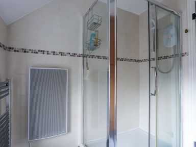 A bathroom with a glass shower enclosure a tiled wall and a heating panel at Gwelfor in Harlech