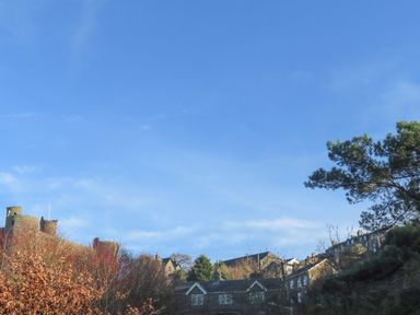 A blue sky above a row of houses with trees and a castle on the left at Gwelfor in Harlech