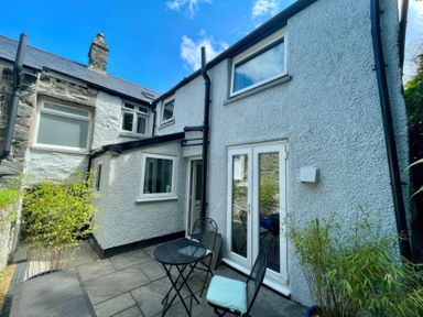 A backyard patio with two chairs and a round table between two buildings with white walls at Gwelfor in Harlech