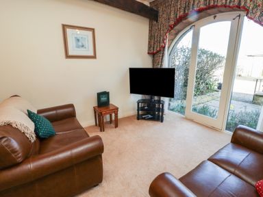 A sitting room with two brown leather sofas a small wooden table and a television by glass doors at Primula Patch in Akeld near Wooler