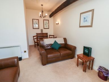 A living room with brown leather sofas a small wooden table and a dining table with chairs at Primula Patch Akeld near Wooler