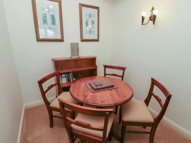 A small dining area with a round wooden table and four chairs a wooden shelving unit with books two framed pictures on the wall and a wall light at Primula Patch Akeld near Wooler