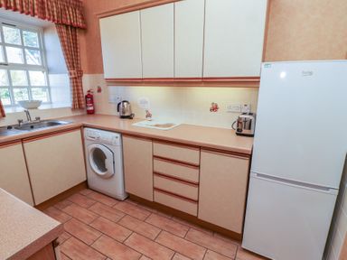 A kitchen with a washing machine fridge toaster kettle sink and checkered curtains at Primula Patch Akeld near Wooler