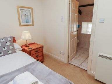A bedroom with a bed pillow lamp and bedside table with an open door leading to a tiled bathroom at Primula Patch in Akeld near Wooler