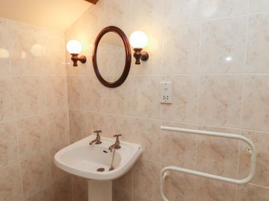 A bathroom corner with a pedestal sink dual taps round mirror and wall lights at Primula Patch in Akeld near Wooler