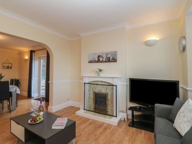 A living room with a fireplace television gray sofa and a coffee table with fruit and wine at Hilltop Cottage in Paignton