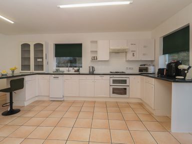 A kitchen with white cabinets black countertops tiled floor and green window blinds at Hilltop Cottage in Paignton