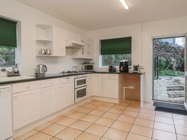 A kitchen with white cabinets and black countertops with appliances and a doorway leading outside at Hilltop Cottage in Paignton