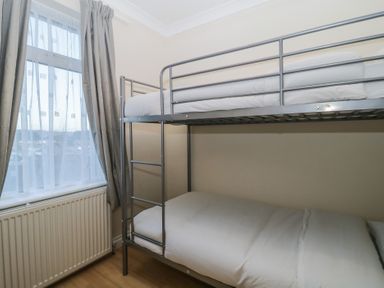 A bedroom with metal bunk beds and a window with curtains at Hilltop Cottage in Paignton
