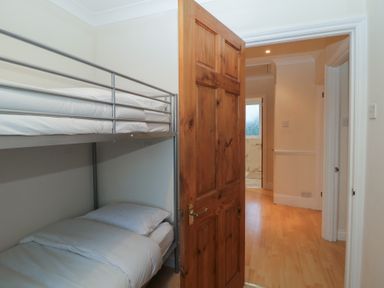 A small bedroom with a metal bunk bed and an open wooden door showing a hallway at Hilltop Cottage in Paignton