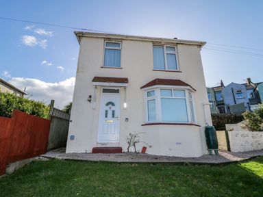 A two-story house with a front door and bay window with a lawn and fences at Hilltop Cottage in Paignton