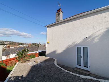 An exterior side view of a white house with a small garden area and a distant view of rooftops at Hilltop Cottage in Paignton