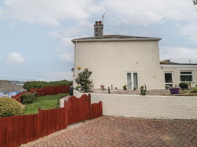 The side view of a cream colored house with a red wooden fence and green lawn at Hilltop Cottage in Paignton