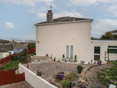 The exterior of a two story house with a gravel garden area and patio furniture at Hilltop Cottage in Paignton