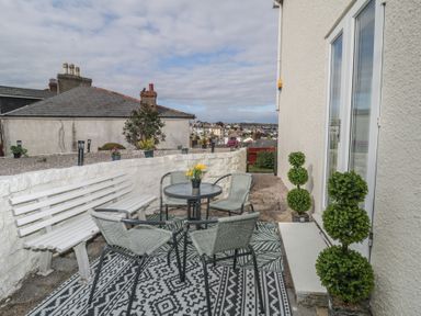 An outdoor patio area with a table and four chairs a white bench and potted plants at Hilltop Cottage in Paignton